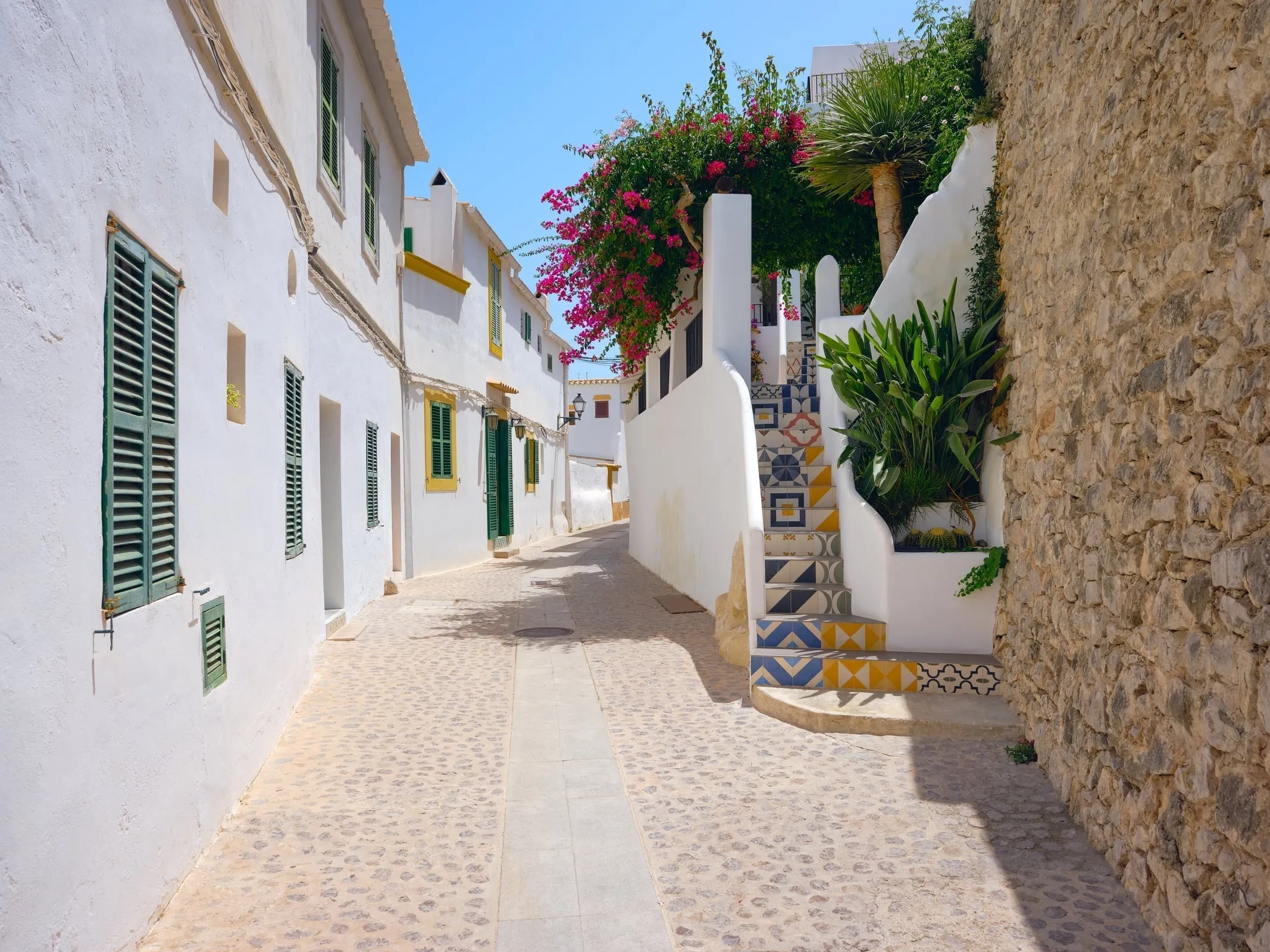 Narrow alleyway in Dalt Vila with purple bougainvillea flowers