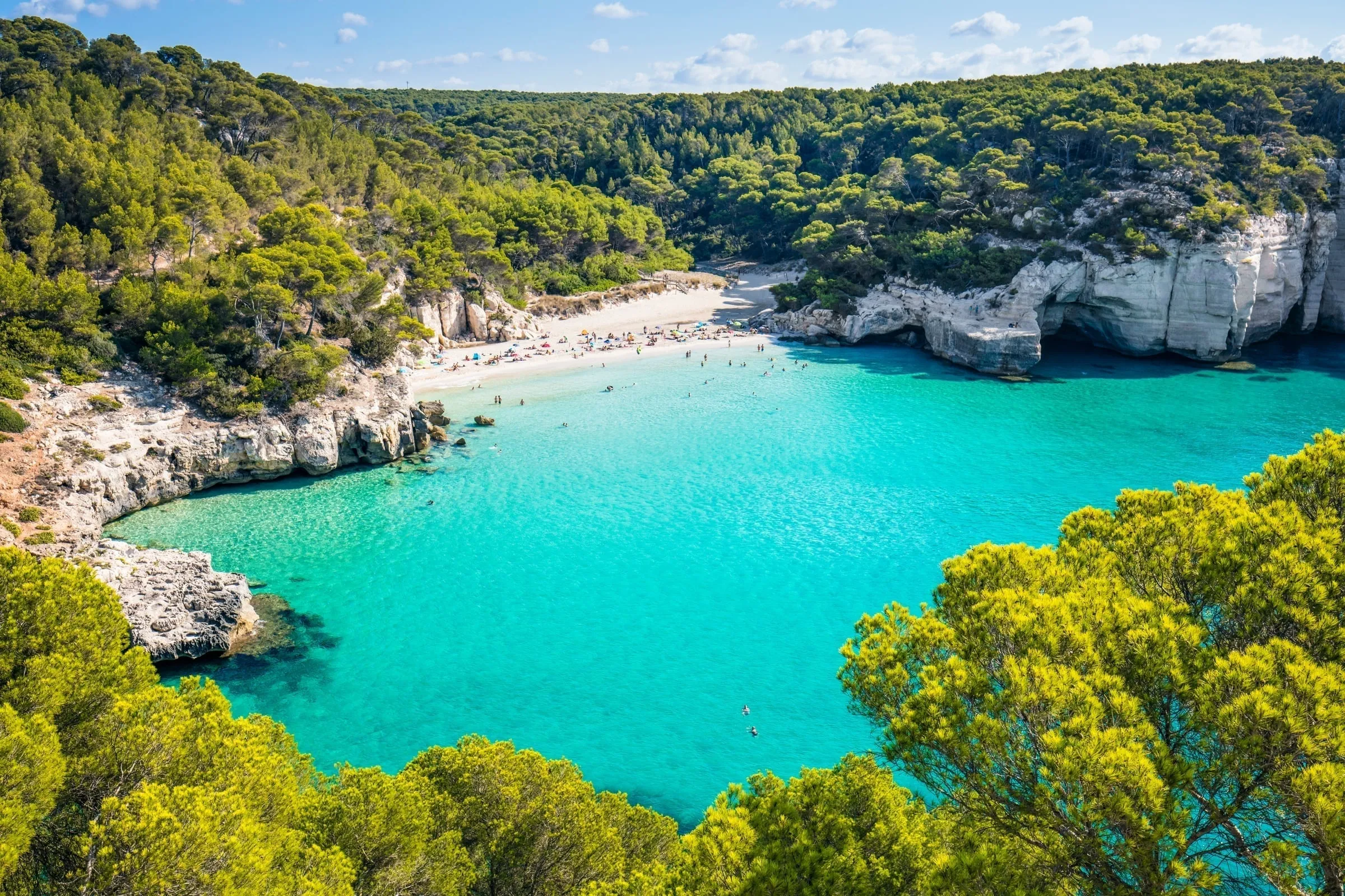 Aerial view of Cala Mitjana showing pristine turquoise waters surrounded by pine forests